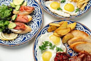 tradicional desayuno platos presentando huevos, salchichas, y varios acompañamientos arreglado artísticamente en un blanco antecedentes foto