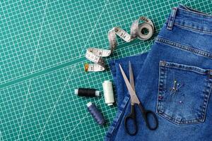 Sewing tools on a cutting mat with denim and thread spools in a craft workspace photo