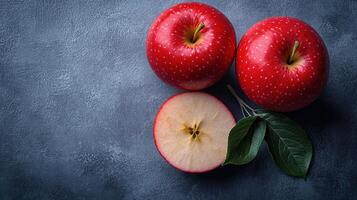 Two vibrant red apples rest on blue backdrop, one sliced in half to show its core photo