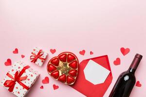 Bottle of red wine on colored background for Valentine Day gift box, envelope and chocolate. Heart shaped with gift box of chocolates top view with copy space photo