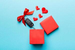 Black car key in a present box with a and red heart on colored background. Valentine day composition Top view photo