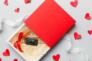 Black car key in a present box with a ribbon red heart on colored background. Valentine day composition Top view photo