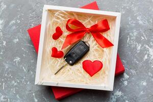 Black car key in a present box and red heart on colored background. Valentine day composition Top view photo