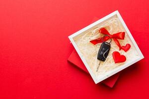 Black car key in a present ribbon and red heart on colored background. Valentine day composition Top view photo