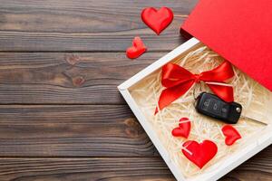 Black car key in a present box with a ribbon red heart colored background. Valentine day composition Top view photo