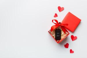 Black car key in a present box with a ribbon and red heart colored background. Valentine day composition Top view photo