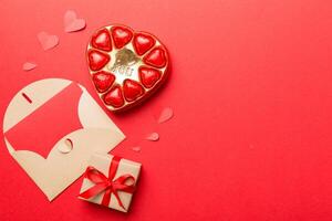Envelope on colored background for Valentine Day gift box and chocolate. Heart shaped with gift box of chocolates top view with copy space photo