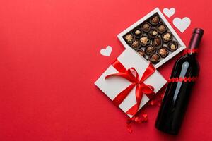 Bottle of red on colored background for Valentine Day with gift and chocolate. Heart shaped with gift box of chocolates top view with copy space photo