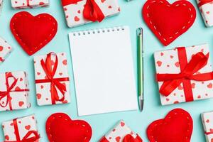 Holiday composition notebook, gift boxes and red textile hearts on colorful background with empty space for your design. Top view of Valentine's Day concept photo