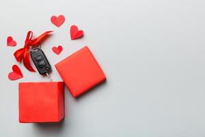 Black car key a present box with ribbon and red heart on colored background. Valentine day composition Top view photo