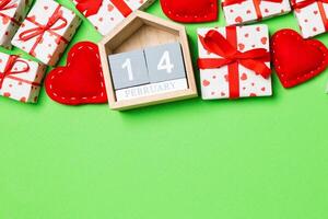 Holiday composition of gift boxes wooden calendar and red textile hearts on colorful background with empty space for your design. The fourteenth of February. Top view of Valentine's Day concept photo
