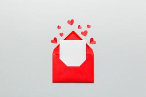 Red paper envelope with empty white card and heart colored background. top view valentines day concept photo