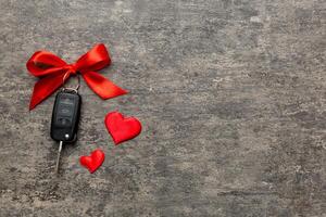 Car key a red bow and a heart on Colored table. Giving present or gift for valentine day or christmas, Top view with copy space photo