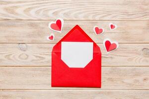 Red paper envelope with empty white card heart on colored background. top view valentines day concept photo