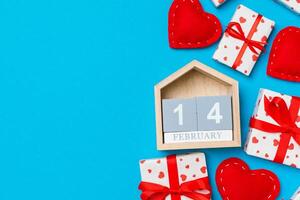 Holiday composition of gift boxes, wooden calendar and red textile hearts on colorful background with empty space for your design. photo