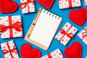 Holiday composition of notebook gift boxes and red textile hearts on colorful background with empty space for your design. Top view of Valentine's Day concept photo