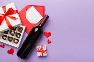 Bottle red wine on colored background for Valentine Day with gift box, envelope and chocolate. Heart shaped with gift box of chocolates top view with copy space photo