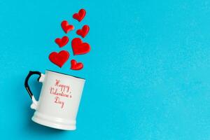 Top view composition of red hearts falling out from cup on colorful background with copy space. Romantic relationship concept. St Valentaine's Day photo
