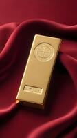 A quiet composition of a single gold ingot placed delicately on a soft velvet surface in rich gold and deep red tones. The background should have empty space for text or branding. photo