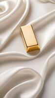 A solitary gold ingot sits on a white silk backdrop, softly lit to create a peaceful ambiance, with space available for text. photo