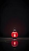 A red lantern rests against a dark background, its reflection softly visible, with room for text in the surrounding space. photo