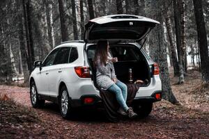White SUV Parked on Forest Path with Woman Resting in Rear Hatch photo