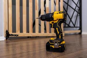 Yellow and Black Cordless Drill with Partially Assembled Baby Gate photo