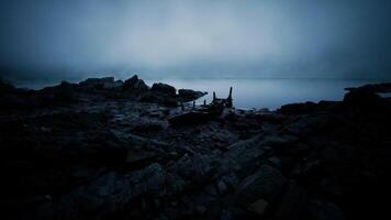 Mysterious fog envelops a lonely boat on a rocky shore at twilight video