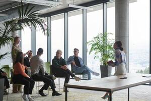 A diverse group of business professionals sits attentively in a modern office, actively participating in a training session led by an instructor, focusing on the latest technological advancements in photo