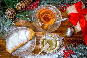 Christmas background, cup of tea with honey and croissant, branch of a Christmas tree in the snow. Top view photo