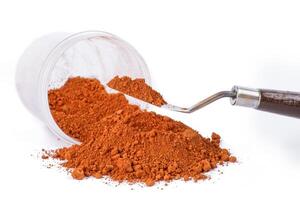 Bright Orange pigment Spice Spilling From Container With Scoop on White Background photo