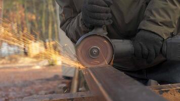 A person wearing gloves operates a cutting tool on a metal piece at an outdoor workshop, creating sparks that illuminate the surrounding forest area in the afternoon light. video