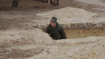 A person digs a large pit in sandy soil using a shovel while surrounded by trees and open space. The activity takes place on a clear day in a rural area. video