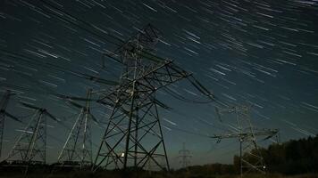 Time lapse of captures star trails swirling above tall power lines in a remote landscape at night, highlighting the contrast between technology and nature's beauty. video