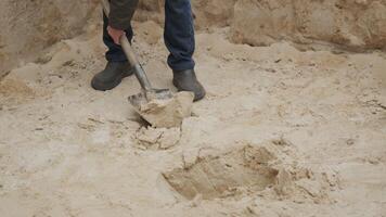 A person is using a shovel to dig into a patch of soft sand, focusing on construction work. The ground is dry and sandy, indicating work taking place outdoors. video