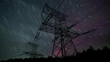 Long-exposure capture showcases star trails and auroras illuminating power lines. The scene is set in a dark area, enhancing the celestial display during the night. video