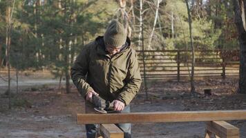 A man in a green jacket handles a steel beam with a power tool in the forest. The serene forest setting reinforces the focus on the work process. video