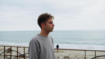 Boy Looks With Neutral Expression Towards The Ocean On A Gloomy Day video