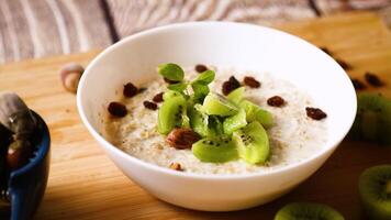 cooked oatmeal with kiwi, honey and nuts in a bowl on a wooden table video