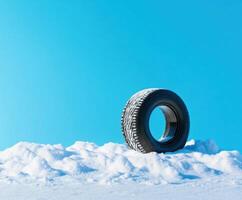 Snow-covered tire resting on white snow under a clear blue sky during winter season photo