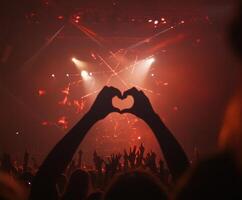 Music lovers celebrate with heart-shaped hands at a vibrant concert under dramatic lighting photo