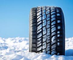 Snow-covered tire resting on a snowy surface under a clear blue sky during wintertime photo