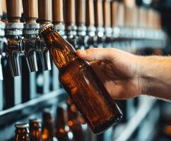 Hand reaching for cold beer bottle at a bar with multiple taps in the background photo