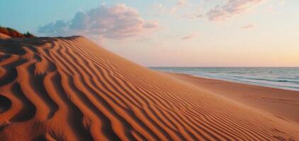 Ripples of sand lead towards towering dune under colorful sky, creating serene beach landscape at sunset. gentle waves add to tranquil atmosphere photo