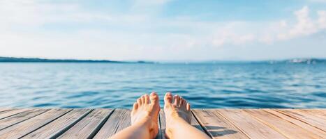 Relaxing view of tanned feet on wooden deck by serene water, evoking sense of tranquility and leisure on sunny day photo