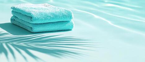 Soft turquoise towels stacked on serene poolside, casting gentle palm leaf shadow. Perfect for relaxation and summer vibes photo