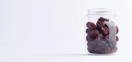 Dried cherries in glass jar on clean white surface, showcasing their rich color and texture. Perfect for healthy snacking or culinary use photo