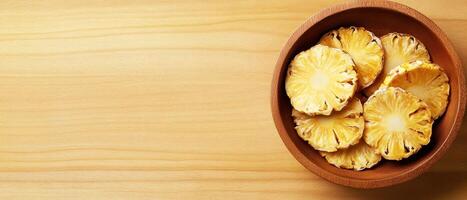 Dried pineapple rings arranged in wooden bowl on light wooden surface, showcasing their vibrant color and texture. Perfect for healthy snacking or decoration photo
