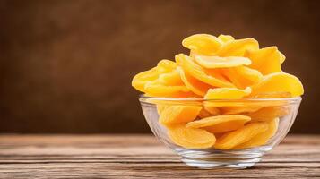Dried mango slices in glass bowl on wooden surface, showcasing their vibrant yellow color and texture. Perfect for snacking or adding to dishes photo