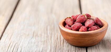 Dried strawberries in rustic wooden bowl on textured wooden surface, showcasing their vibrant color and natural appeal. Perfect for healthy snacking or culinary use photo